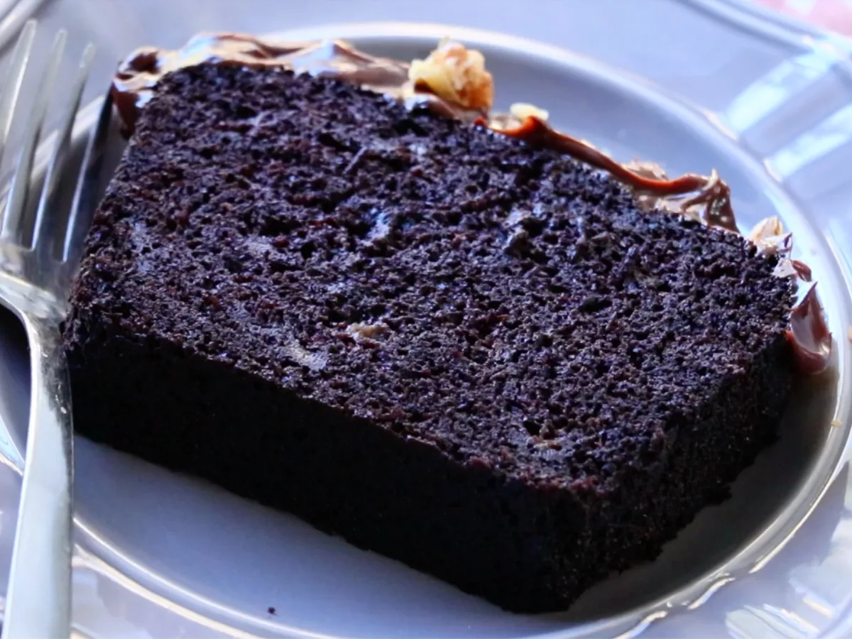 A slice of moist chocolate banana cake with ganache on a gray plate