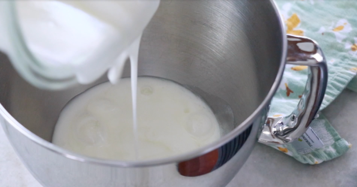 pouring heated sugar and egg white in a mixing bowl