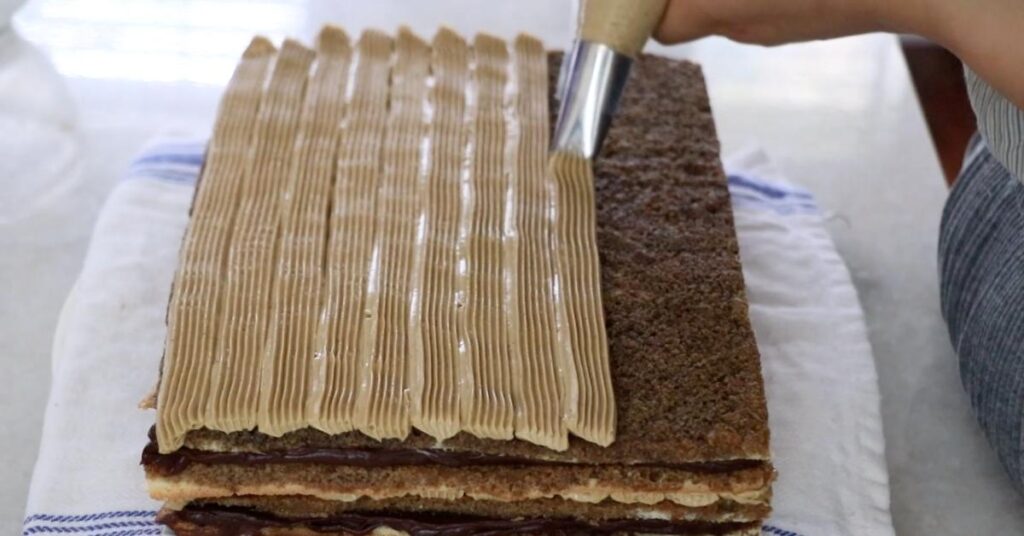 piping mocha buttercream on top of biscuit sponge to assemble a opera cake