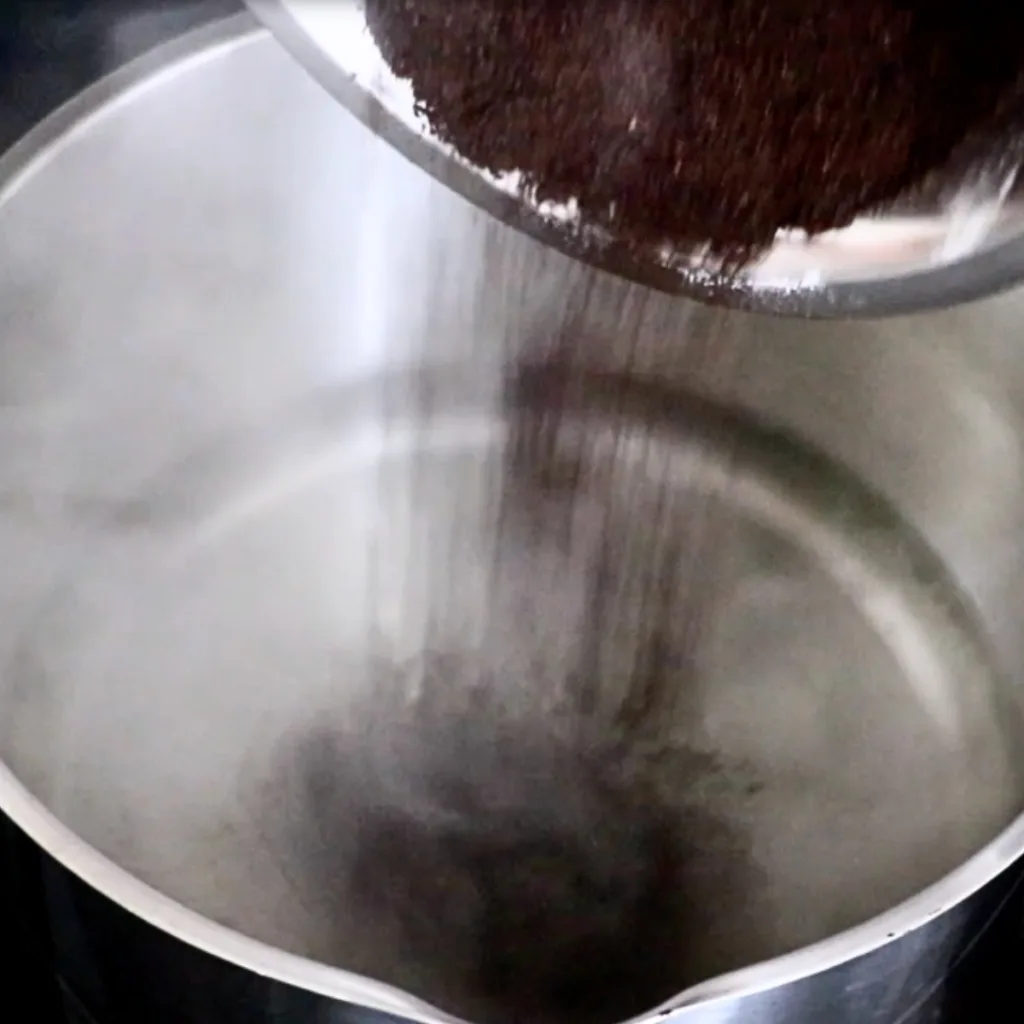 adding ground coffee in hot water