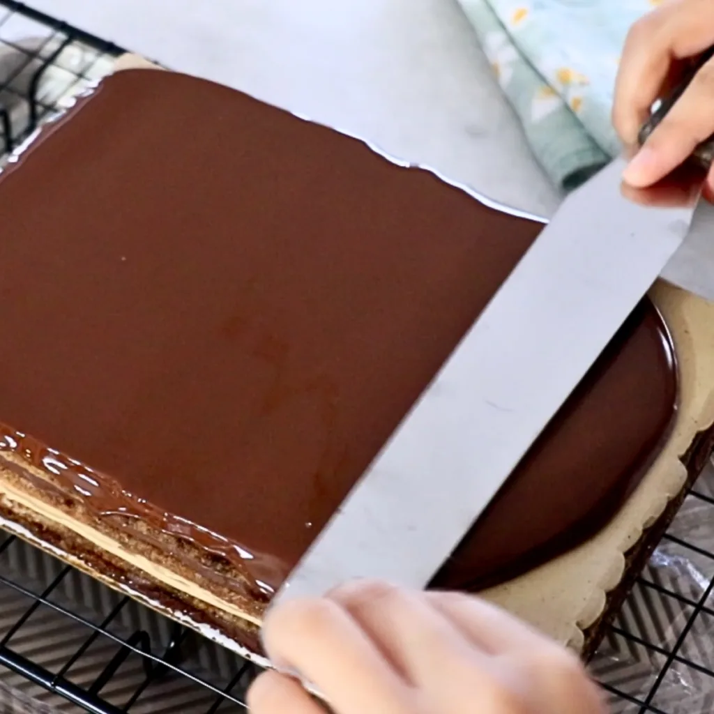 spreading chocolate glaze on top of opera cake