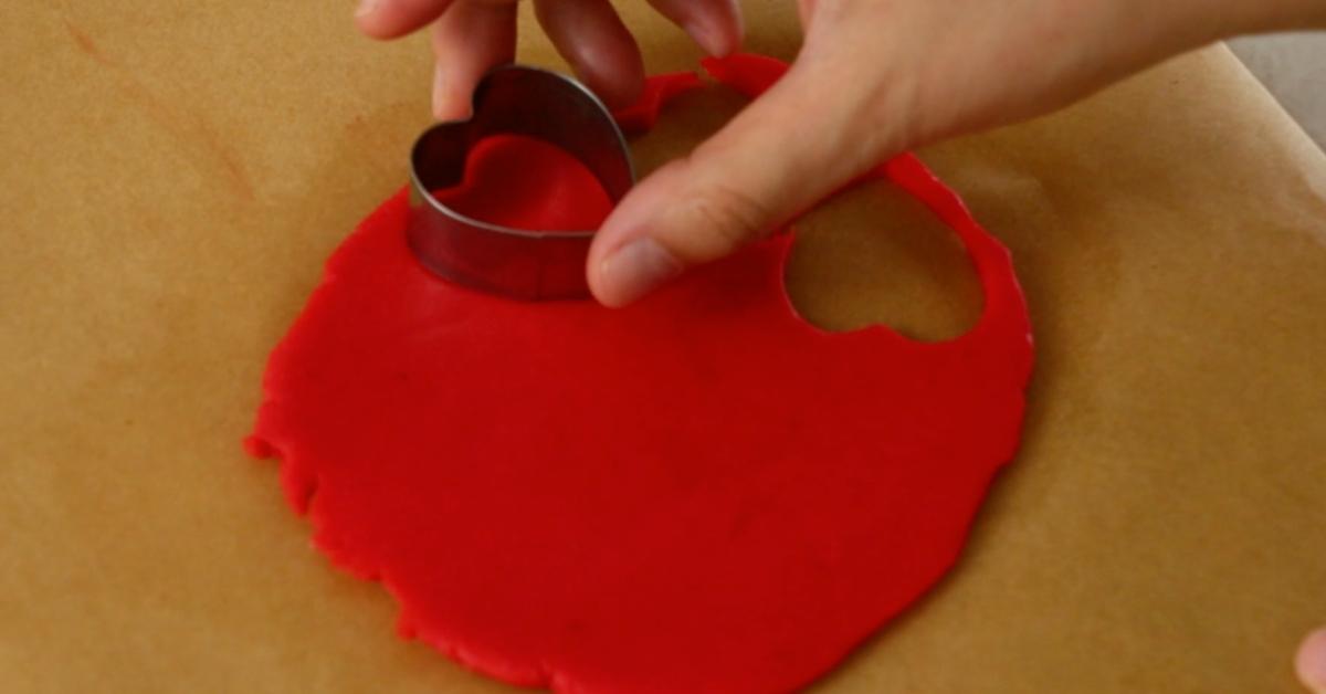 cutting red dough with a heart cookie cutter