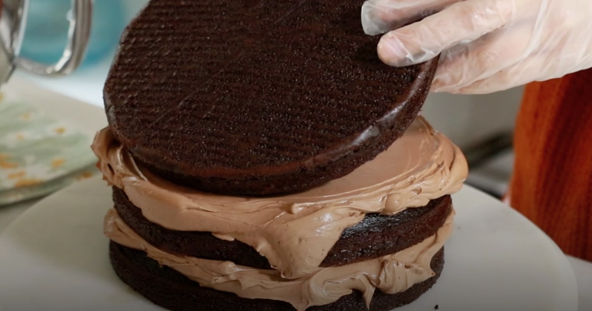 placing a 3rd layer of a chocolate cake on top of buttercream to frost a cake