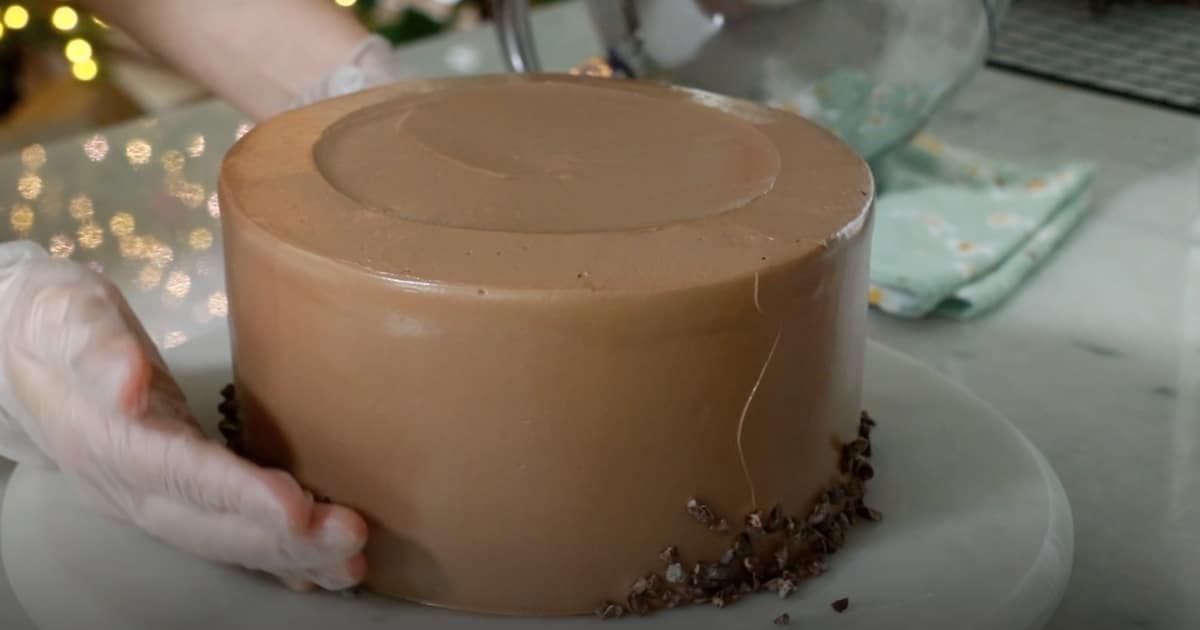 attaching cacao nibs on the side of a whole chocolate cake
