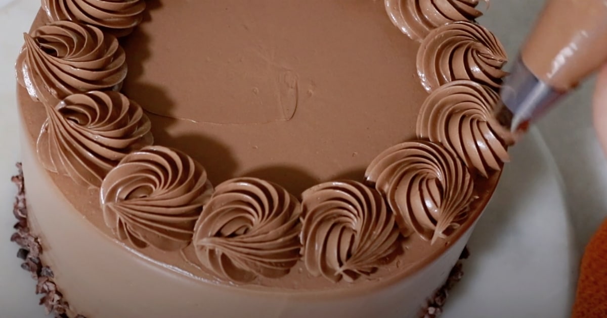 piping basic swirls with buttercream on top of a whole chocolate cake