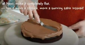 spreading a chocolate buttercream evenly with a spatula on top of a chocolate cake