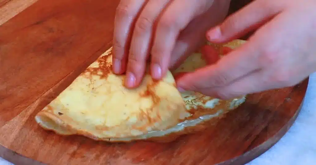folding a crepe filled with whipped cream and strawberries