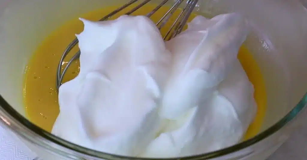 adding meringue to yolk mixture to make fluffy strawberry cream cake