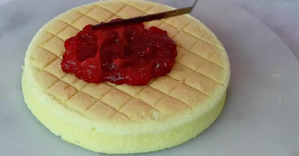 spreading strawberry jam on top of sponge to make strawberry cream cake
