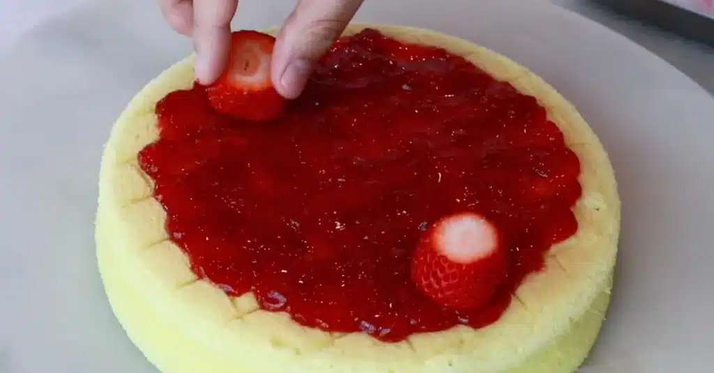 attaching fresh strawberries on strawberry jam to make strawberry cream cake