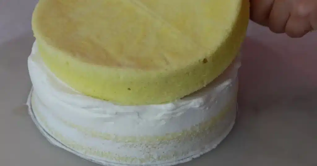 placing 2nd layer of sponge on a cake spreading whipped cream on sponge to make strawberry cream cake