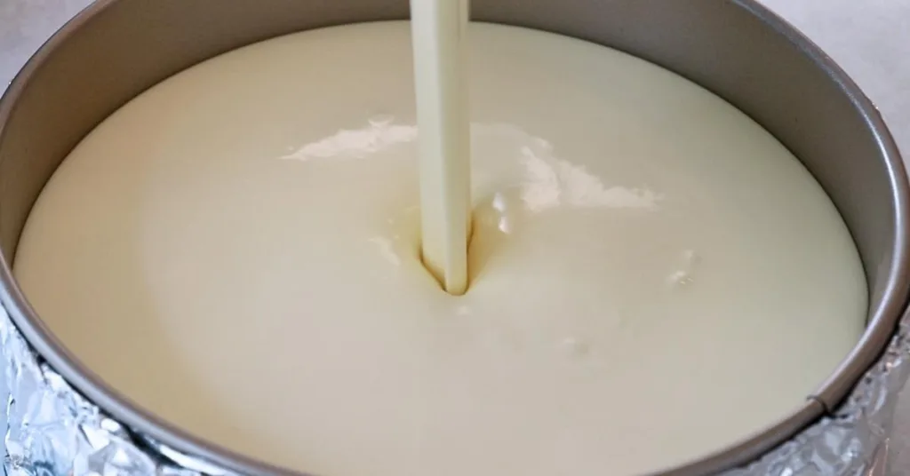 pouring cheesecake batter into a pan