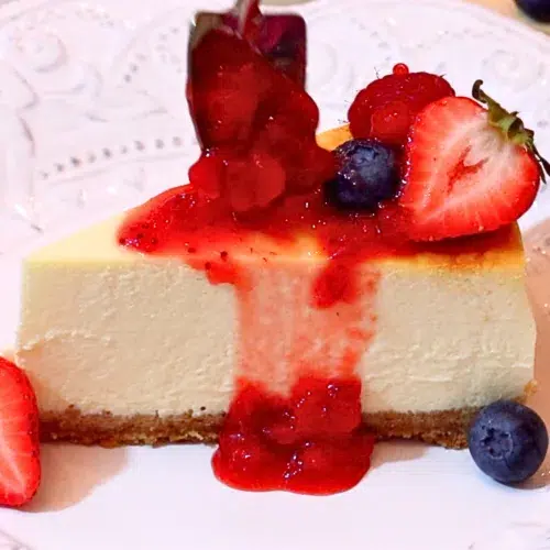 a slice of baked cheesecake with strawberry sauce and fresh fruits