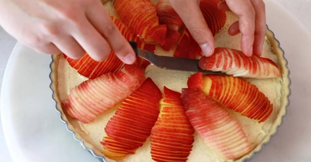 assembling fresh peaches on almond cream to make peach tart