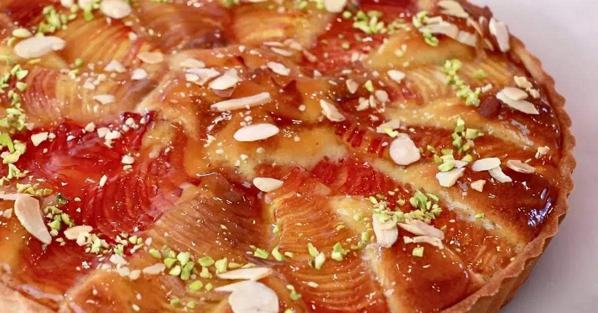 a close-up of a almond peach tart coated with apricot jam glaze, almond slices and pistachios