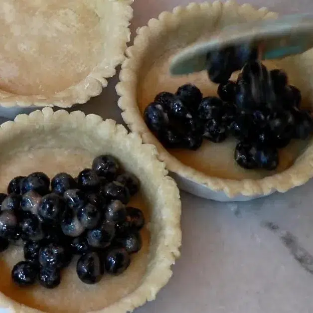 adding blueberry pie filling to pie dough