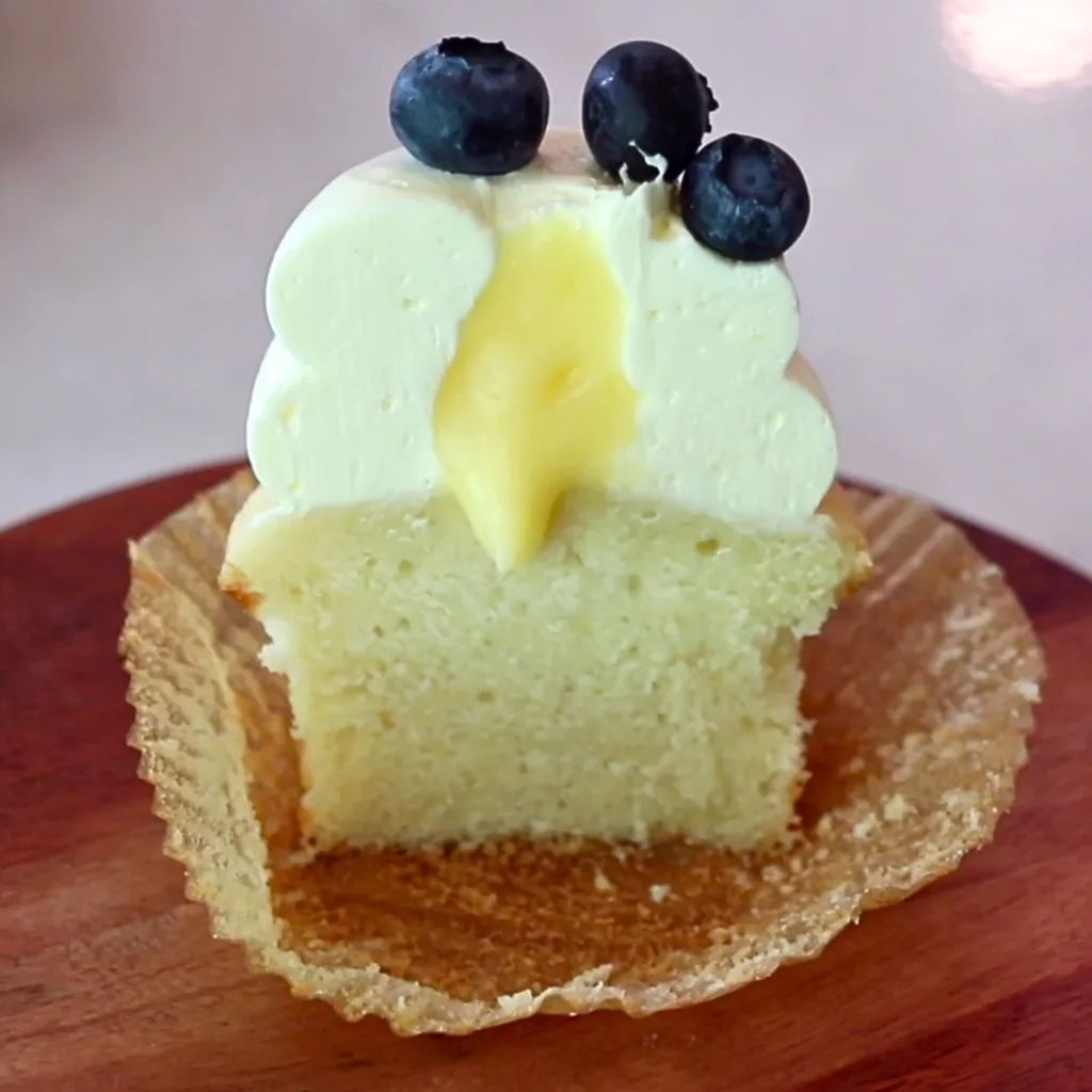 a lemon cupcake with lemon frosting and blueberries on top, cut in half