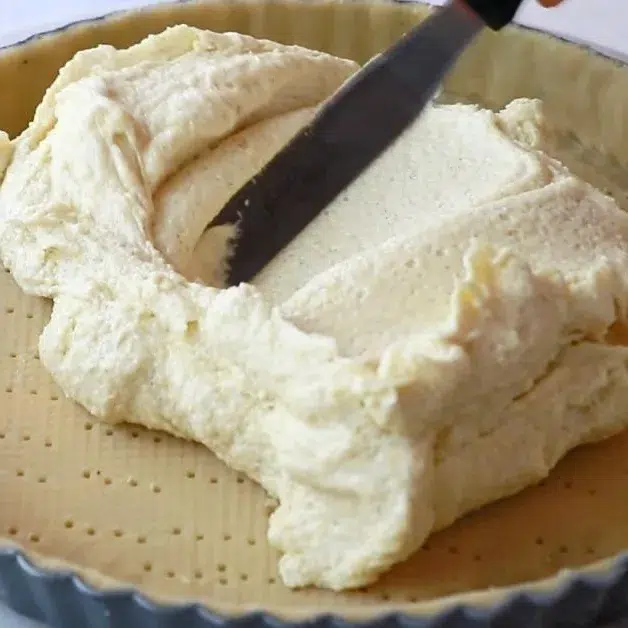 spreading almond cream over a tart to make almond peach tart