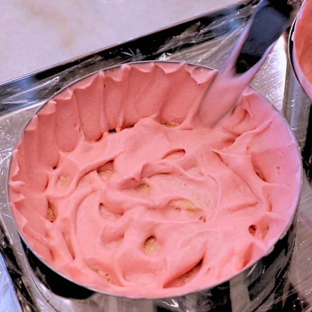coating the side of a cake ring with mousse to assemble a raspberry mousse cake