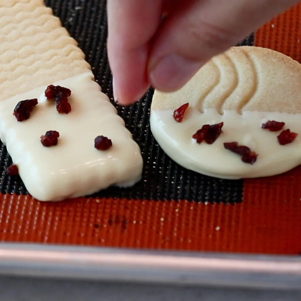 sprinkling dried cranberries on top of white chocolate on a cookie