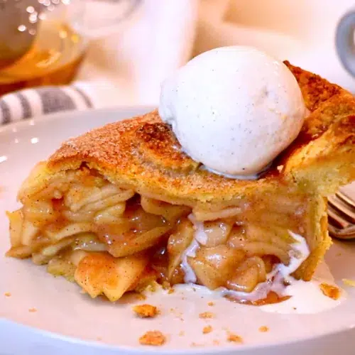 a slice of homemade apple pie with vanilla ice cream on top on a plate
