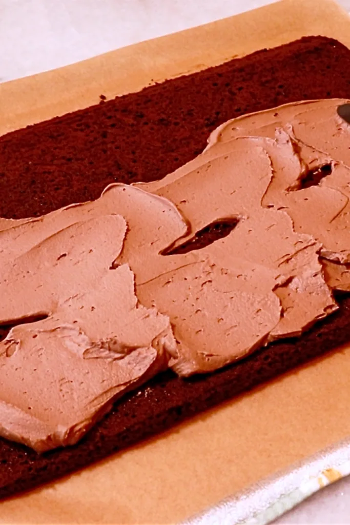 spreading chocolate cream onto a chocolate sponge cake to make buche de noel